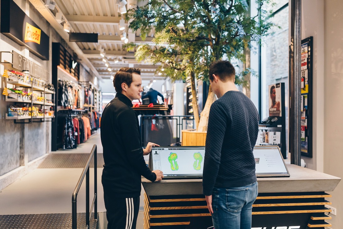 Medewerker van All4Running bespreekt de uitkomst van een loopanalyse met een klant op een digitaal scherm